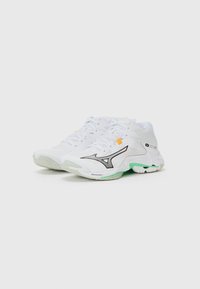 White athletic shoes with a textured surface, black accents, green soles, and orange detailing. Designed for comfort and performance.