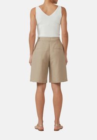 Shorts en lin beiges taille haute avec une coupe décontractée, dotés de deux poches arrière, associés à un débardeur blanc ajusté en v.