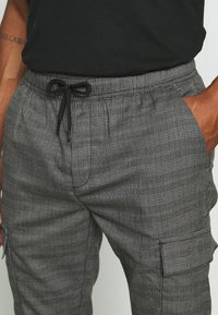 Grå rutiga cargo byxor med elastisk midja, dragsko, sidofickor och en texturerad tyg. Har subtila linjer och mönster.