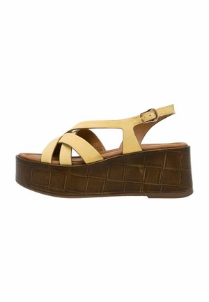 Gele suède platform sandalen met gekruiste bandjes, een bruine, getextureerde sleehakzool en een verstelbare enkelband voor een stevige pasvorm.