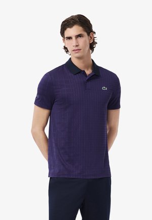Polo shirt viola con un motivo a griglia testurizzata, maniche corte e colletto nero. Presenta un piccolo logo verde sul petto.