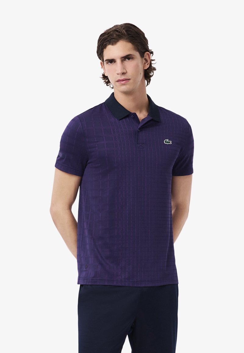 Polo shirt viola con un motivo a griglia testurizzata, maniche corte e colletto nero. Presenta un piccolo logo verde sul petto.
