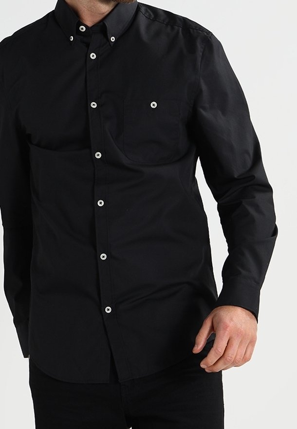Camicia nera con colletto, maniche lunghe e taschino. Presenta bottoni bianchi e una texture di cotone liscia.