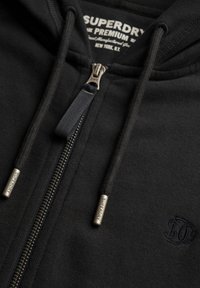 Felpa nera con zip realizzata in tessuto morbido, caratterizzata da una finitura testurizzata, cordini regolabili e dettagli del gancio brandizzati. Logo ricamato in evidenza.