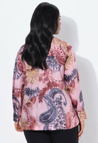Langärmliges Hemd aus pinkfarbigem Stoff mit einem Paisleymuster in Rot, Blau und Gelb, mit glatter Textur und Knopfakzenten an den Bündchen.
