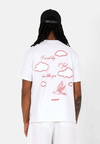 Witte katoenen t-shirt met rode wolk- en vogelafbeeldingen, met de tekst: "Ik ben niet verlegen. Ik vind je gewoon niet leuk." Gedrukt logo aan de onderkant.