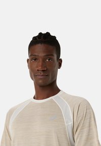 T-shirt de sport beige avec des manches courtes texturées et des accents en maille blanche. Arbore un logo discret sur la poitrine et un col rond.