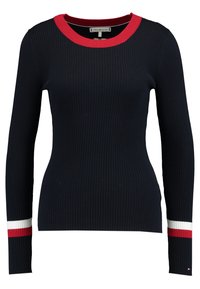 Pull côtelé bleu marine à manches longues avec col rond rouge et rayures accentuées rouge et blanc aux poignets. Présente une silhouette ajustée.