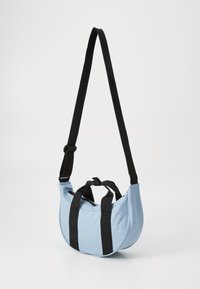 Sac à bandoulière bleu clair en tissu avec des sangles en toile noires. Présente une forme arrondie et une poignée en haut pour des options de transport polyvalentes.
