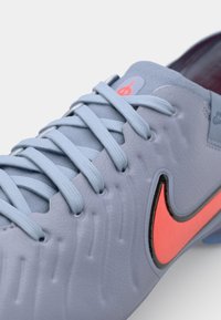 Light blue soccer shoe with textured synthetic material, flat laces, and a bright orange Nike swoosh logo on the side.