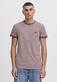 Camiseta de manga corta color marrón con un cuello y remates de manga en un marrón oscuro en contraste; presenta un pequeño logo negro en el pecho.