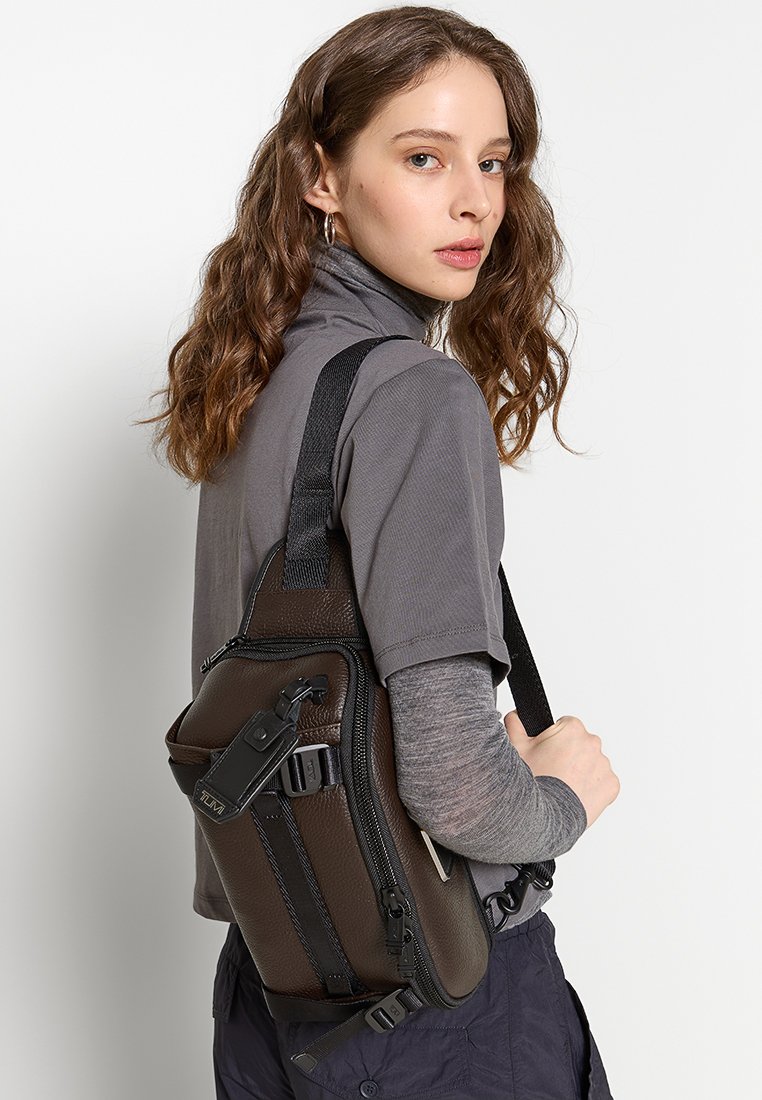 Braune Leder-Schultertasche mit strukturierter Oberfläche, ausgestattet mit einem Reißverschluss, verstellbarem Trageriemen und schwarzen Hardware-Akzenten.