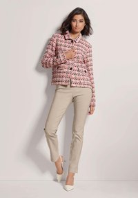 Roze tweed jasje met een kraag, dubbelknopsluiting en multikleurige garen. Gecombineerd met beige nauwsluitende broek en witte puntige hakken.