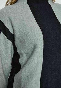 Pletena turtleneck pulover s barvnim blokom, ki vključuje svetlo sivo in temno sivo sekcijo, gladko teksturo in sproščen kroj.