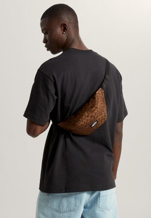 Sac banane imprimé léopard en tons marron, présentant une forme incurvée, une sangle noire ajustable et un logo visible à l'avant.