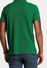 Grön pikétröja i strukturerad tyg med kort krage. Baksidan har sidosprund och matchas med jeans.