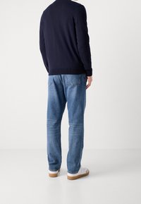 Marinblå tröja med rundad halsringning, strukturvävt tyg, kombinerad med ljusblå denimjeans med avslappnad passform och synliga sömmar.