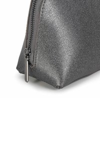 Grå tekstureret kosmetikpose med en trekantet form, der har en sølvfarvet lynlås og en glat bundkant. Tekstureret overflade med en subtil glans.