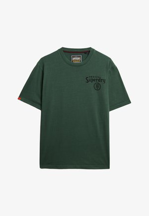 T-shirt in cotone verde con maniche corte, scollo tondo, stampa del logo frontale e un'etichetta rossa accentata sulla manica sinistra. Tessuto morbido.