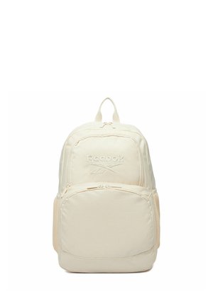 Cream-colored Reebok backpack with top handle, front zip pocket, mesh side pockets, and embroidered logo on a white background.