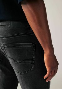 Jeans din denim negru au buzunare spate cu un design ușor curbat. Talie include o etichetă din piele neagră cu inscripția "DENIM SUPPLY Co." embosată.