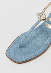 Sandal din denim albastru, cu un design cu curea subțire, vârf pătrat și accente de hardware aurie cu logo-ul "REPLAY". Material texturat și detalii cusute.
