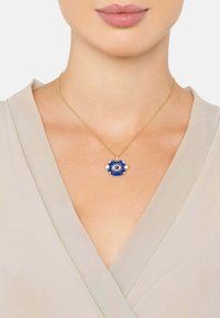 Collana in oro con pendente rotondo blu decorato con un design a occhio, accentuato da piccole stelle dorate su uno sfondo beige chiaro.