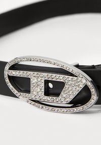 Black leather belt featuring an oval silver buckle decorated with clear rhinestones, showcasing an intricate design and smooth texture.