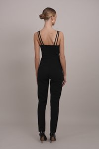 Črni kombinezon z več tankimi naramnicami, oprijetim pasom in krojenimi hlačami. Gladek material in minimalni detajli z okovji.