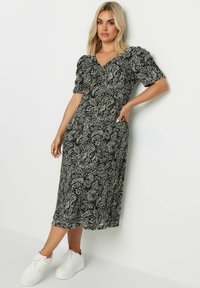 Svart och vit paisleymönstrad midiklänning med korta puffärmar och sidofickor, kombinerad med vita sneakers för en avslappnad look.