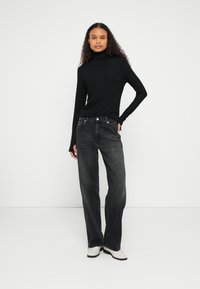 Czarna bluzka z długim rękawem i golfem, zestawiona z ciemnoszarymi szerokimi jeansami o wysokim stanie i pięciokieszeniowym kroju. Całość dopełniają białe buty.