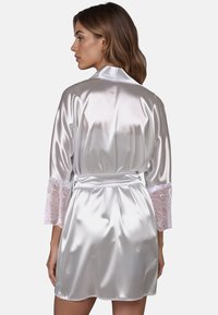 Rochie de satin albă cu mâneci lungi, având dantelă la mansete, legată la talie și cu o textură netedă și lucioasă.