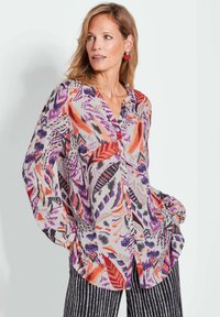 Blouse à manches longues ornée d'un motif floral et de feuilles vibrant en violet, rouge et orange sur un fond clair. Design à boutons à l'avant, ourlet arrondi.