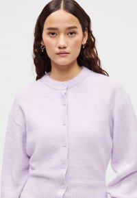 Λιλά πουλόβερ με στρογγυλή λαιμόκοψη, κουμπιά μπροστά και ριμπ μανσέτες. Κατασκευασμένο από μαλακό υλικό με υφή.