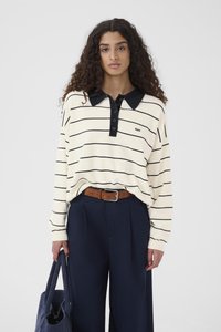 Polo de manga larga a rayas en crema con rayas negras y cuello, combinado con pantalones anchos azul marino y cinturón marrón, sosteniendo un bolso azul.