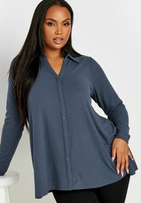 Mörkblå skjorta med knappar, ribbad textur, lång ärm och krage. Lätt utställd design vid fållen.