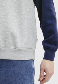 Grå og marineblå sweatshirts med farveblok, ribbede manchetter og kant; blødt, struktureret stof; hånd delvist synlig holder denimstof.