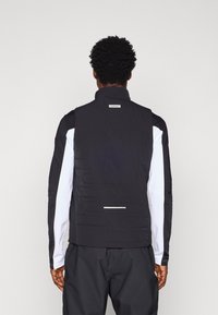 Mustvalge spordivesti, millel on kõrge krae, tekstureeritud selg ja peegeldav triip. Valmistatud kergest kangast, long suknotega.