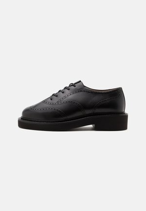 Schwarzer Leder-Brogue-Schuh mit Schnürverschluss, dekorativen Perforationen und dicker Sohle mit niedrigem Absatz, von der Außenseite gezeigt.