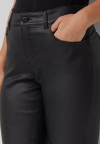 Mustad faux nahk püksid siledat tekstuuri, esiküljel on tasku ja vööl nuppe sulgemiseks.