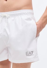 Λευκά μαγιό βερμούδα με ελαστική μέση και κορδόνι. Διαθέτει πλαϊνές τσέπες και γκρι λογότυπο EA7 στο αριστερό πόδι. Λεία υφή.