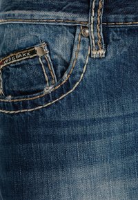 Denim jeans in een vervaagde blauwe kleur. De zak heeft contrasterende beige stiksel en een klein label, met een ronde zilveren knoop.