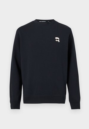Sweat-shirt noir à manches longues avec col rond, avec un petit graphique blanc représentant une personne portant des lunettes de soleil sur la poitrine.