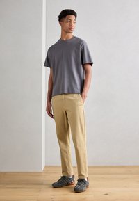 Gray cotton t-shirt with short sleeves, paired with light beige chinos and gray sneakers with orange accents. Standing on a wooden floor.