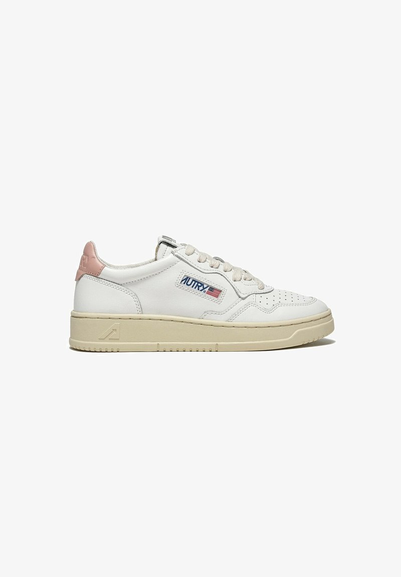 Sneaker bianca in pelle con accenti beige, punta perforata e linguetta sul tallone rosa chiaro. Presenta un'etichetta con logo e lacci piatti su una suola robusta.