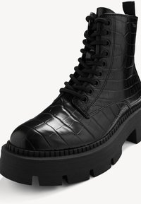 Botte de combat à talon haut noire avec texture crocodile, semelle épaisse à crampons et avant à lacets.