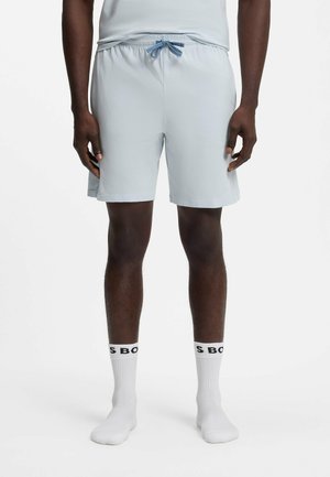 Mann trägt hellgraue Shorts mit Kordelzug und weiße Sportsocken mit schwarzem Text vor neutralem weißem Hintergrund.