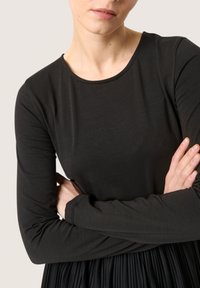 Black long-sleeve top with a round neckline, made of soft material. The fabric fits snugly, with smooth texture and subtle seams.