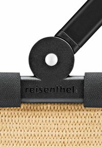 Composant de fixation noir avec un détail circulaire blanc, attaché à un tissu tissé beige, avec un marquage en relief sur un bord.