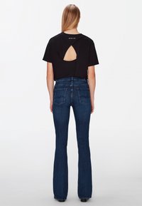 Black cropped t-shirt with a back cutout, paired with dark blue flared jeans featuring stitched pockets and a fitted waist.